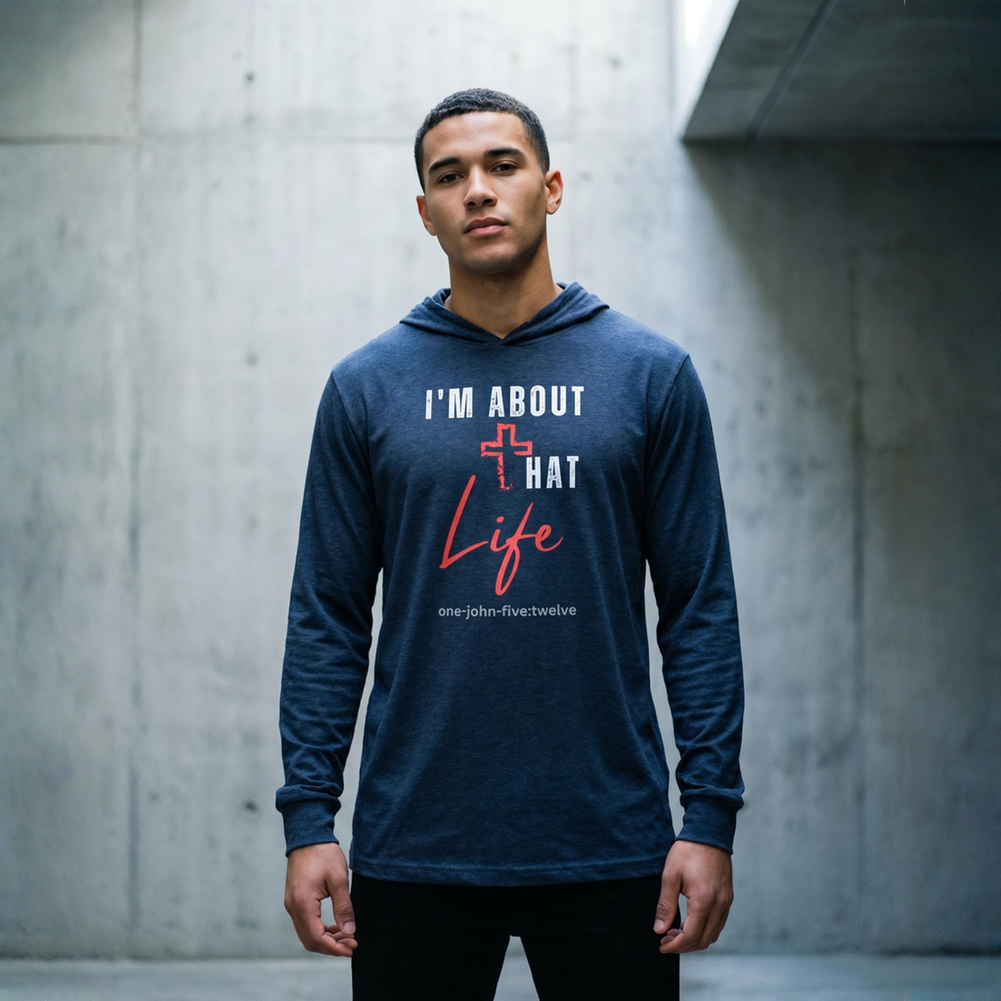 Man wearing a blue hoodie t-shirt with text 'I'm About That Life' standing near a concrete wall.