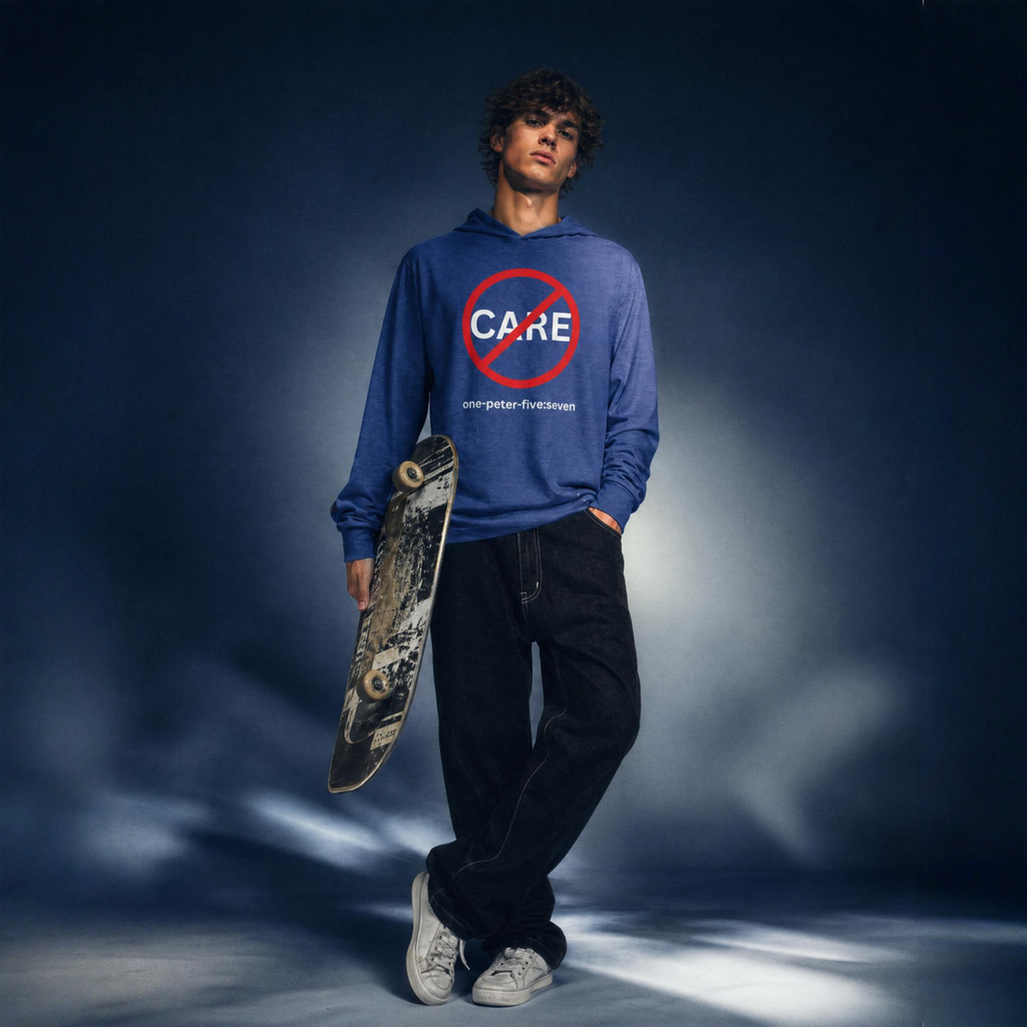 Person wearing a blue hoodie t-shirt with a 'Don't Care' logo, holding a skateboard against a dark background