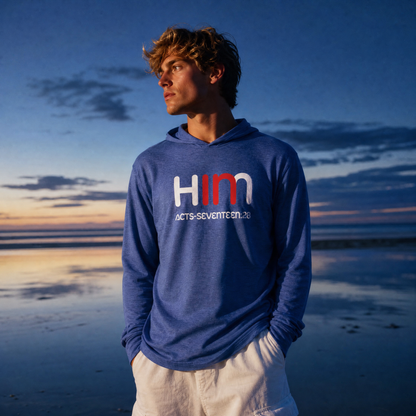 Person wearing a blue hoodie with text "In Him" standing on a beach at sunset.