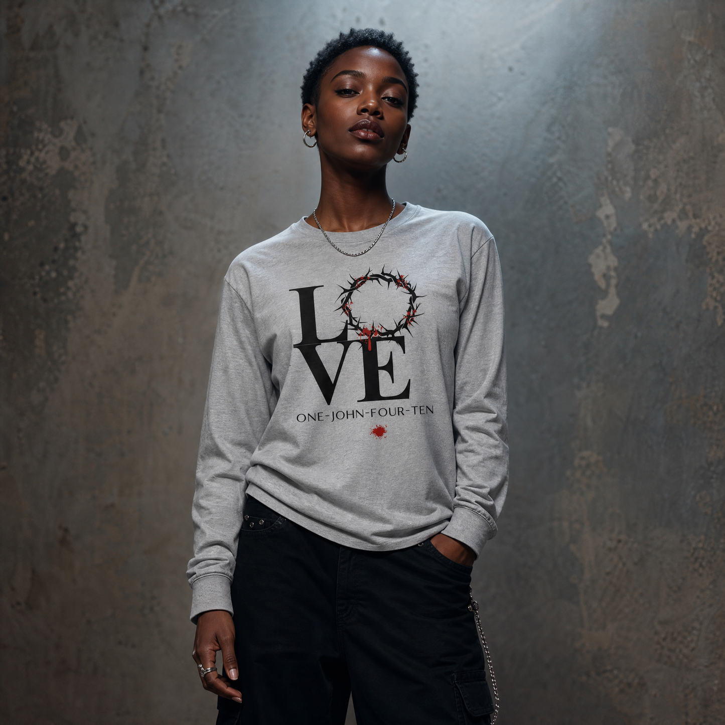 Model is wearing a gray long sleeve t-shirt with text 'LOVE' and a graphic of the crown of thorns in place of the 'O' standing in front of a gray wall.