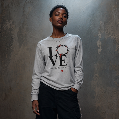 Model is wearing a gray long sleeve t-shirt with text 'LOVE' and a graphic of the crown of thorns in place of the 'O' standing in front of a gray wall.