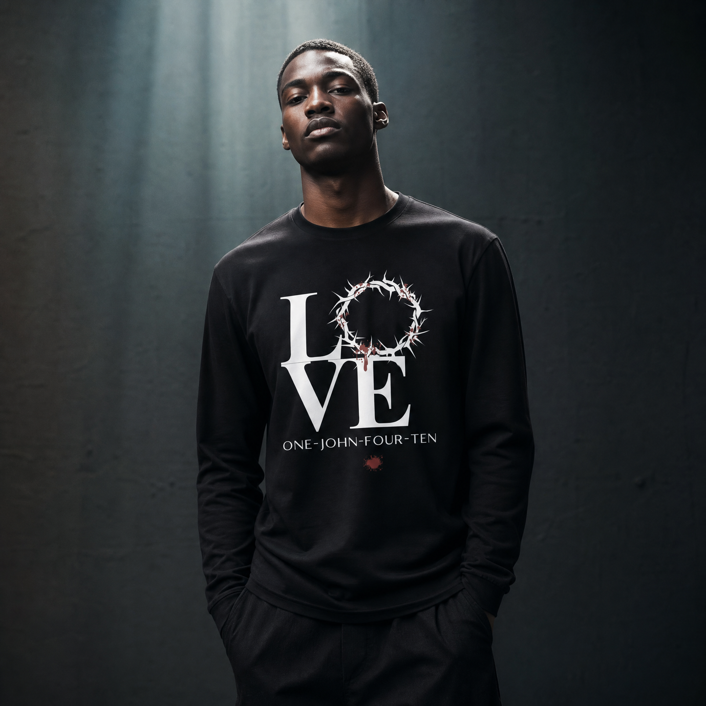 Model is wearing a black long sleeve t-shirt with text 'LOVE' and a graphic of the crown of thorns in place of the 'O' standing in front of a gray wall.