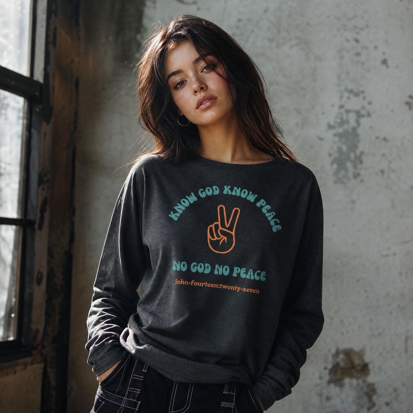 Person wearing a dark gray t-shirt with text 'Know God Know Peace, No God No Peace' with a peace symbol design standing against a gray background
