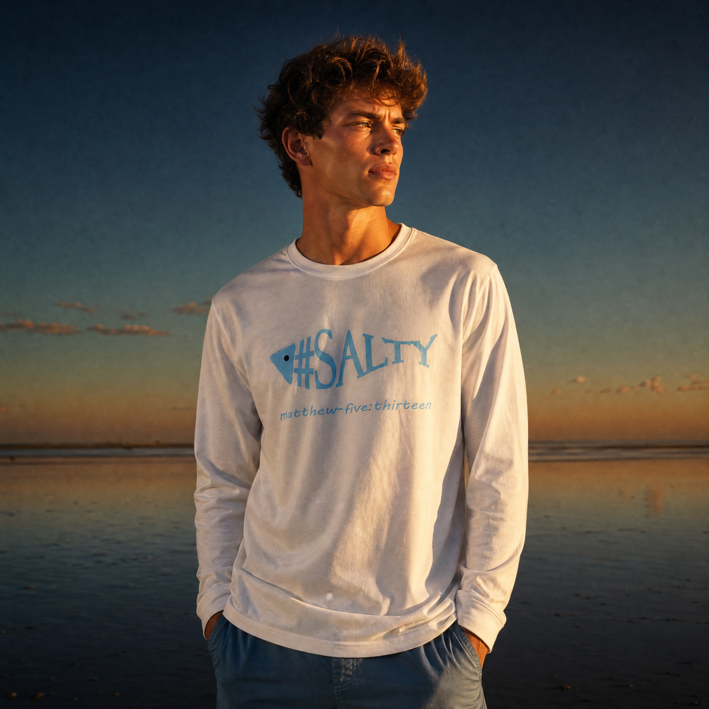 Man wearing a white '#SALTY' t-shirt on a beach at sunset
