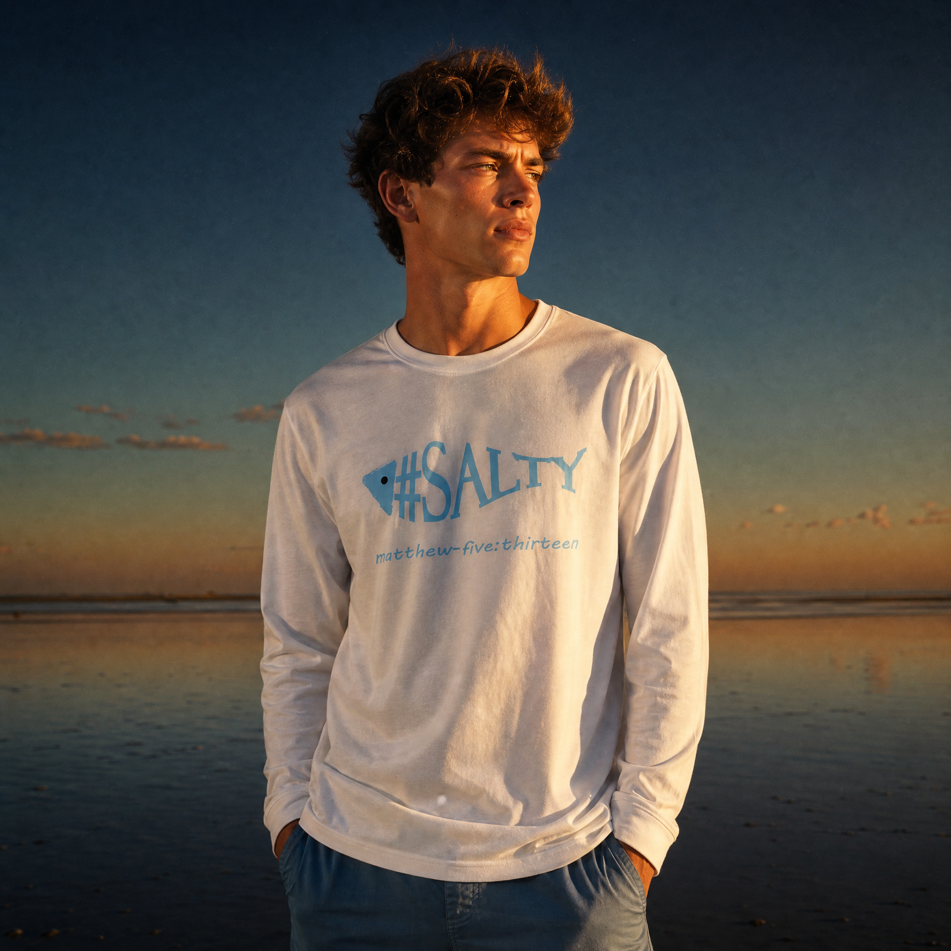 Man wearing a white '#SALTY' t-shirt on a beach at sunset