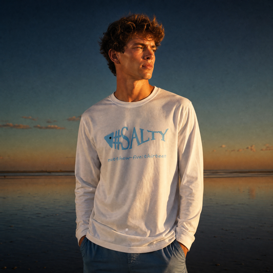 Man wearing a white '#SALTY' t-shirt on a beach at sunset