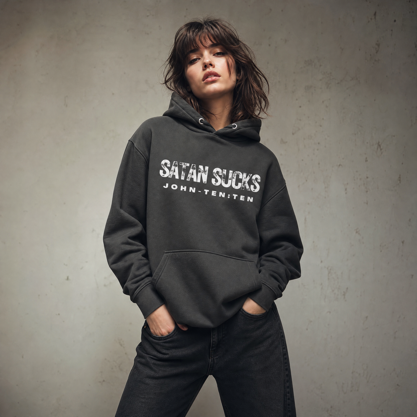 Model wearing a vintage black hoodie with the text 'SATAN SUCKS' printed in white across the chest, posed against a textured gray concrete wall.