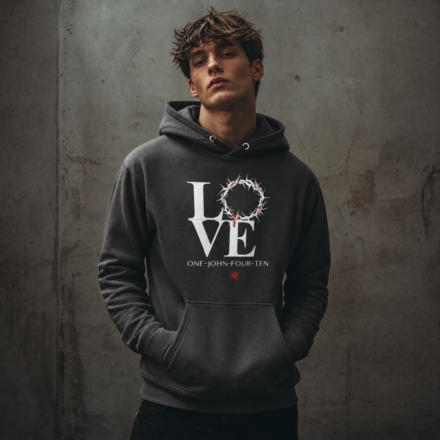 Model is wearing a vintage black hoodie with text 'LOVE' and a graphic of the crown of thorns in place of the 'O' standing against a gray wall.