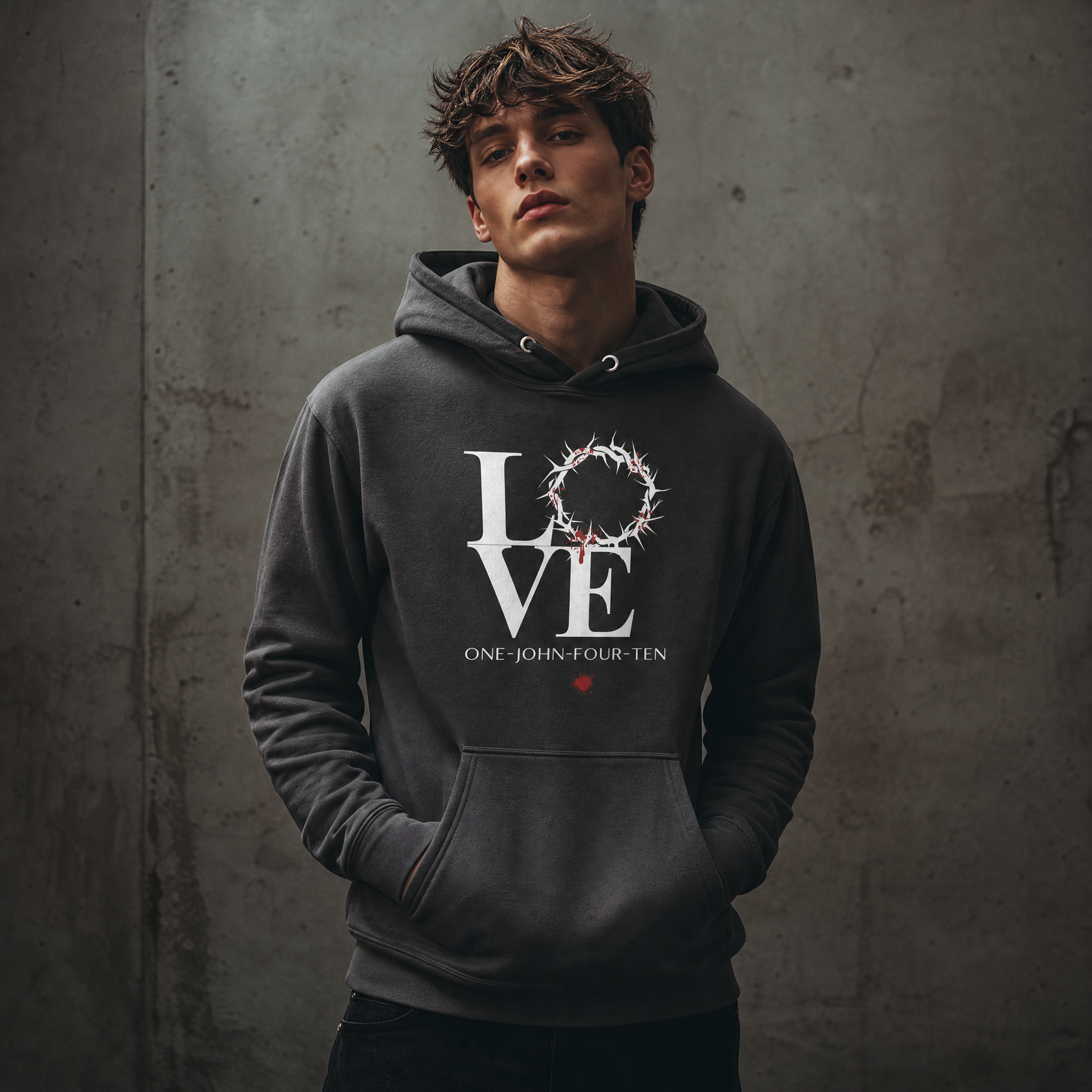 Model is wearing a vintage black hoodie with text 'LOVE' and a graphic of the crown of thorns in place of the 'O' standing against a gray wall.