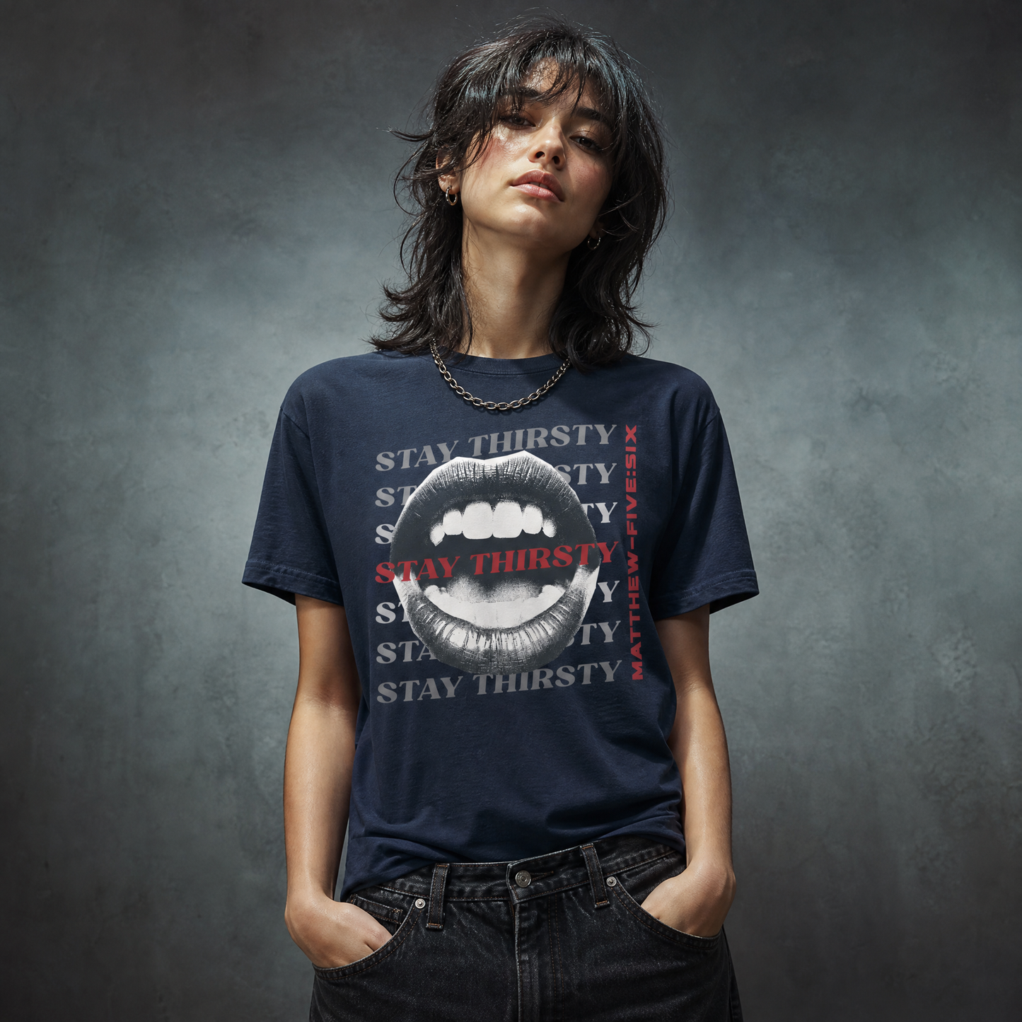 Model wearing a navy blue t-shirt with text 'Stay Thirsty' and an open mouth graphic; standing against a concrete wall
