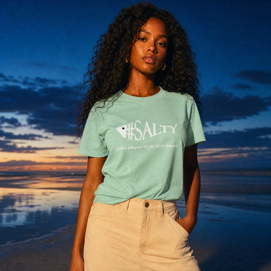 Model is wearing a heather mint green '#SALTY' t-shirt standing on the beach at sunset