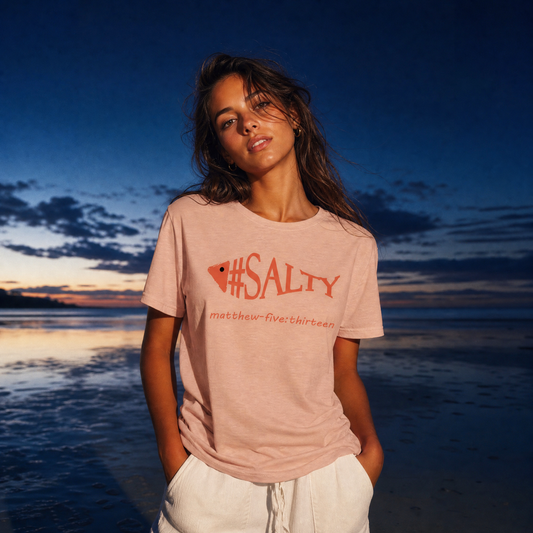 Person wearing a '#SALTY' t-shirt by a body of water at sunset