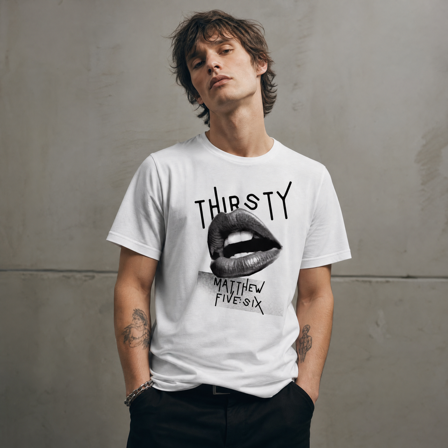 Person wearing a white t-shirt with text 'Thirsty' and a graphic; standing against a concrete wall.