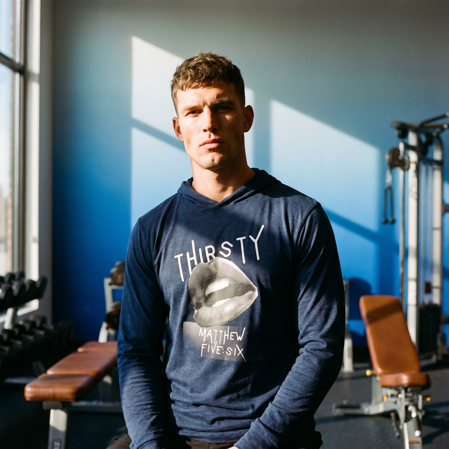 Person wearing a navy blue t-shirt hoodie with text Thirsty and a graphic of an open mouth, in a gym setting