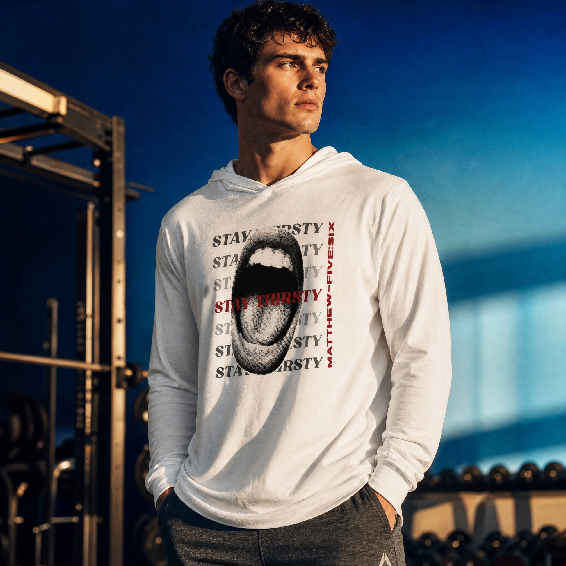 Person wearing a white t-shirt hoodie with graphic design of a wide open mouth and text Stay Thirsty, standing in a gym.