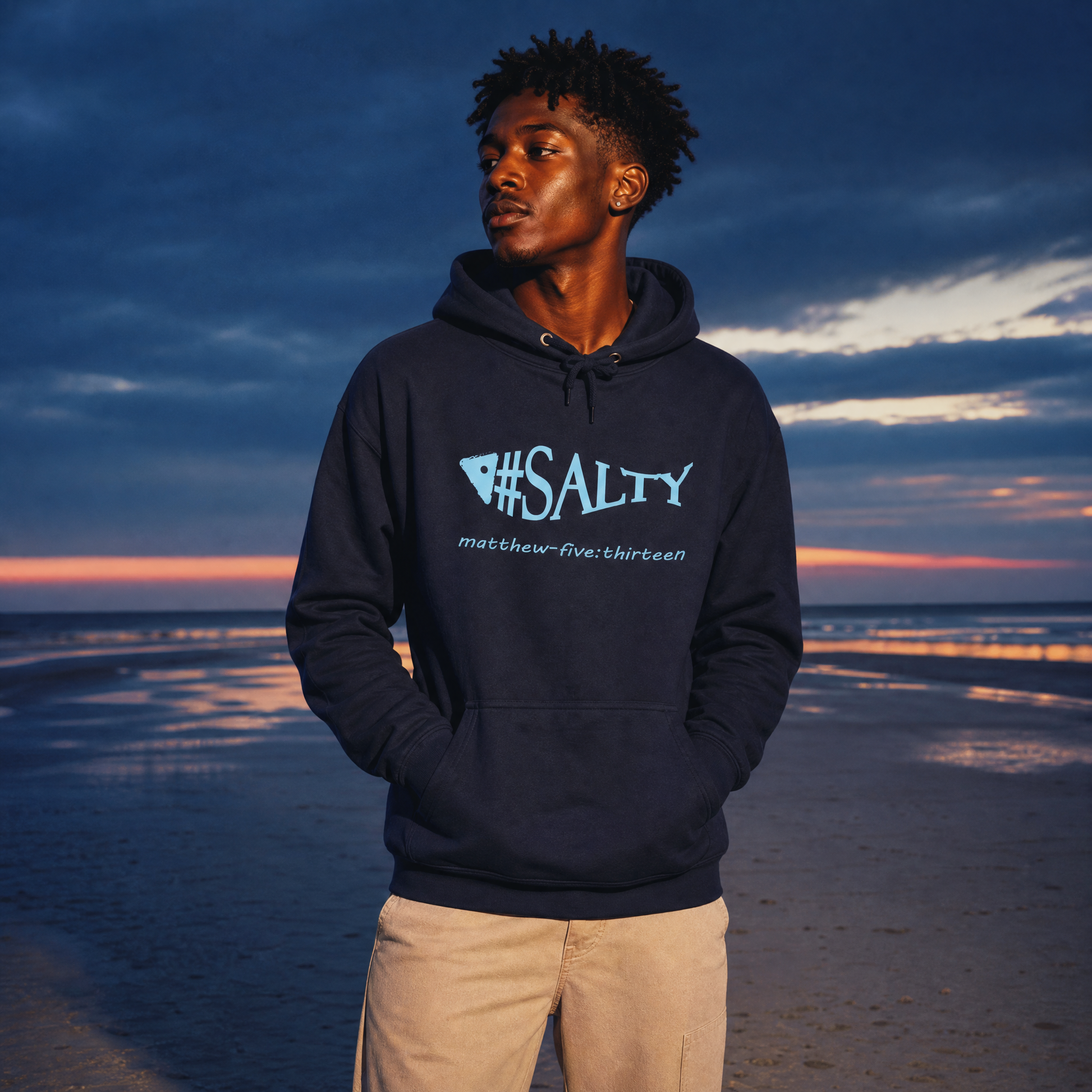 Person wearing a hoodie with '#SALTY' text standing on a beach at sunset