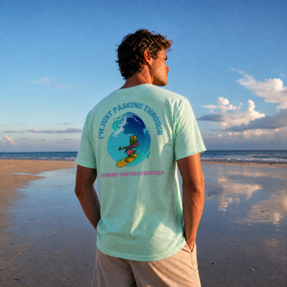 Man standing on the beach wearing a heather mint green t-shirt with a graphic  of a surfing alien with the words I'm Just Passing Through 
