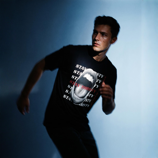 Person wearing a black t-shirt with text Stay Thirsty and graphic of a wide open mouth against a blue background